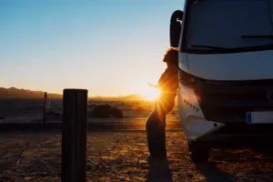 Happiness and freedom life with woman against camper van and golden sunset in background. People enjoying vanlife and summer holiday vacation with big camping car parked off road. Alone female traveler enjoy nature